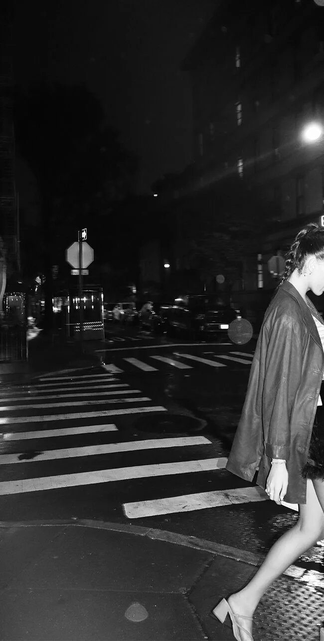 Black-and-white night street scene with a figure at a city crosswalk