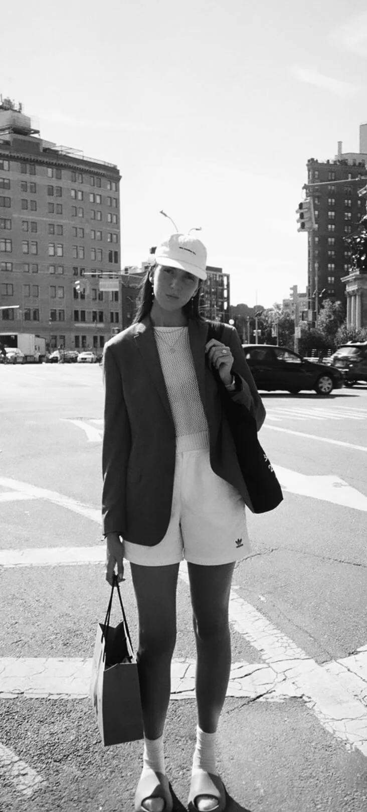 Black-and-white street-style shot of a woman in a cap on a city crosswalk